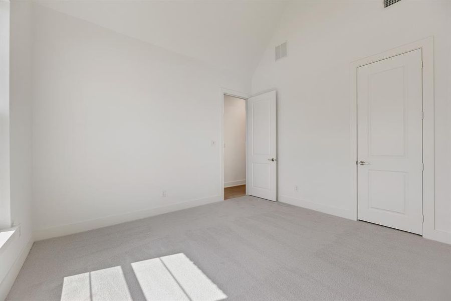 Unfurnished bedroom featuring light carpet and high vaulted ceiling
