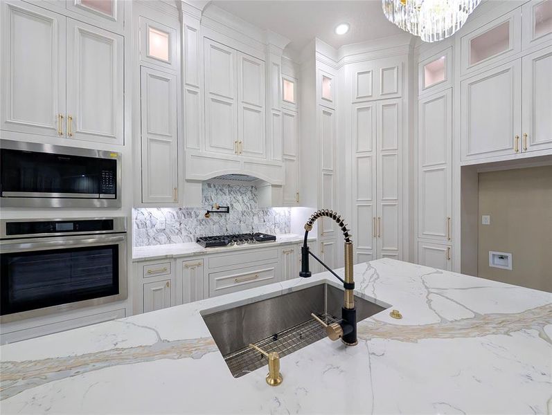 Kitchen with appliances with stainless steel finishes, light stone counters, tasteful backsplash, and white cabinets