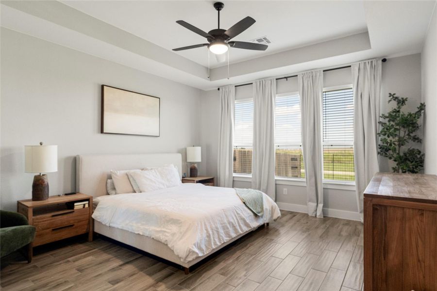 Relax in this tranquil bedroom, featuring a tray ceiling, ceiling fan, and elegant wood-look tile flooring. Relax in this tranquil bedroom, featuring a tray ceiling, ceiling fan, and elegant wood-look tile flooring.