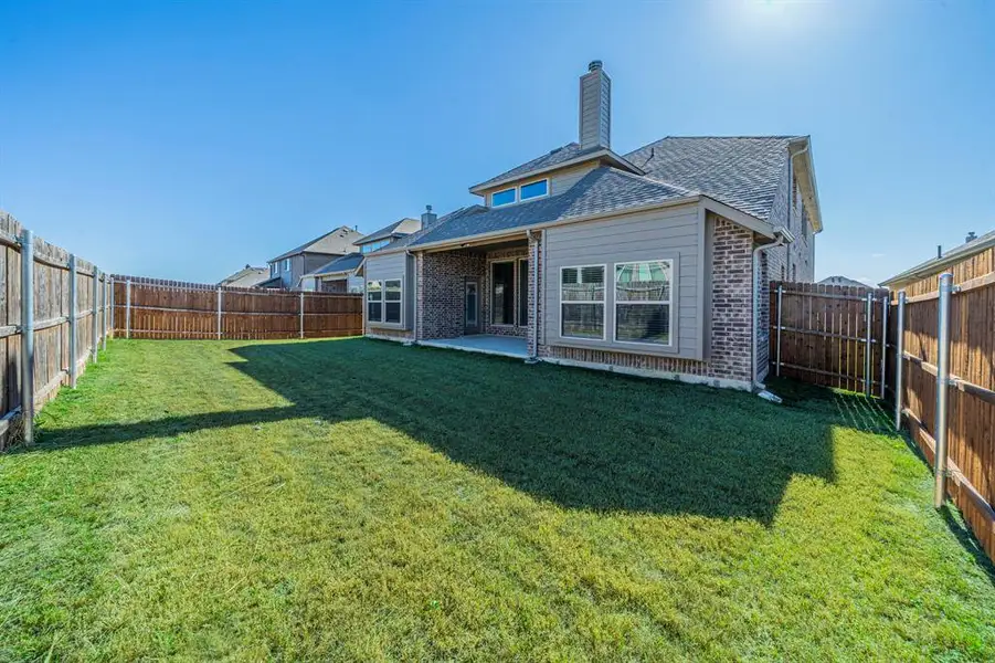 Expansive fenced backyard featuring a verdant lawn and a covered patio