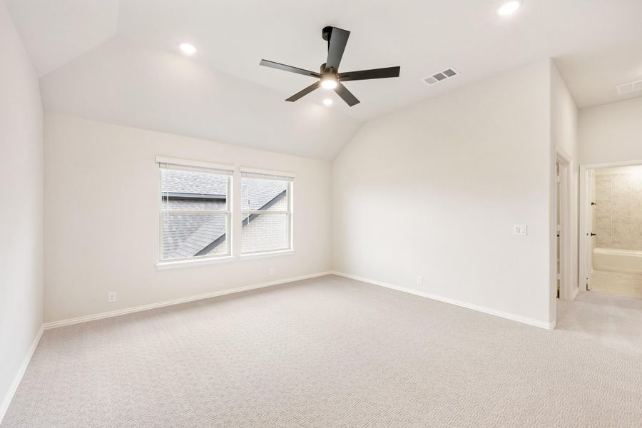 Empty bedroom with vaulted ceiling, ceiling fan, carpet flooring, and ensuite bathroom doorway