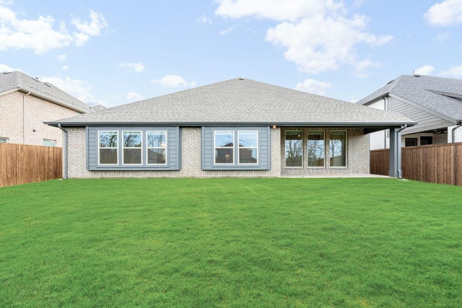 Rear view of single-story brick home with gray siding, large windows, and fenced backyard with green lawn