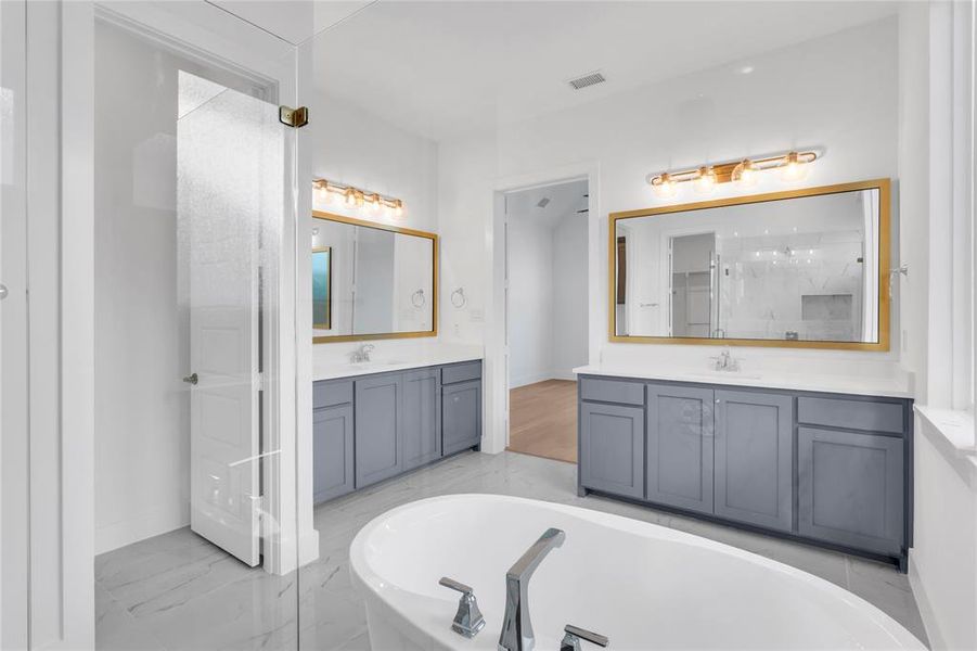 Full bath featuring a freestanding tub, two vanities, light marble finish floors, and a marble finish shower