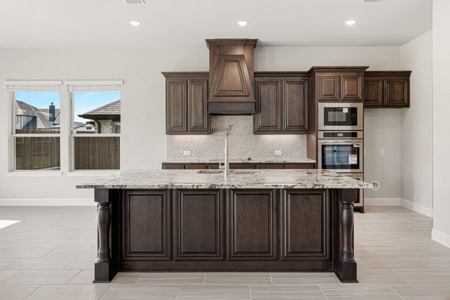 Kitchen with dark wood cabinets, granite island, custom range hood, and built-in stainless steel appliances Kitchen with dark wood cabinets, granite island, custom range hood, and built-in stainless steel appliances