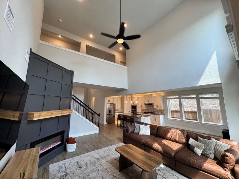 Living room with a glass covered fireplace, wood finished floors, ceiling fan, stairway, and a high ceiling