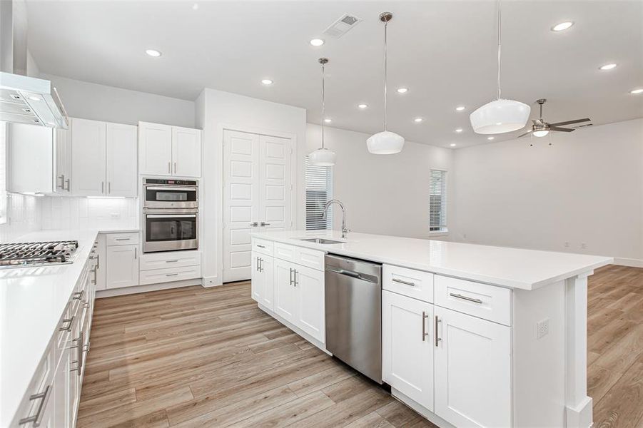 Kitchen featuring hanging light fixtures, white cabinets, wall chimney range hood, recessed lighting, and stainless steel appliances