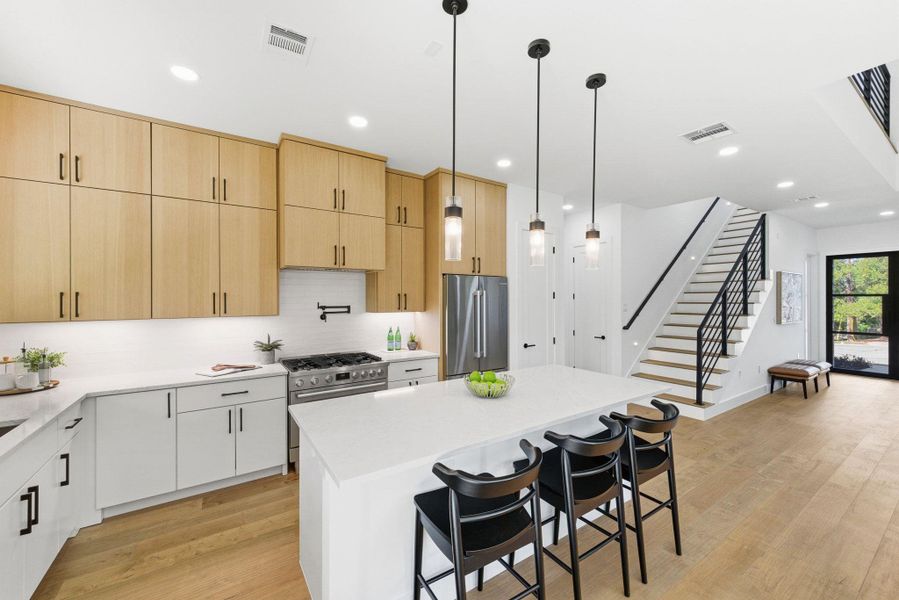 Kitchen with light brown cabinets, decorative light fixtures, light wood-style flooring, a kitchen breakfast bar, and appliances with stainless steel finishes plus center island