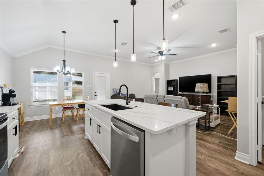 Kitchen featuring stainless steel dishwasher, light stone countertops, arched walkways, white cabinetry, and ornamental molding