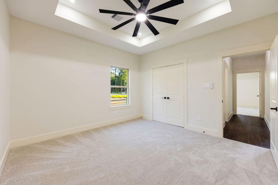 This spacious secondary carpeted bedroom features a modern ceiling fan and recessed lighting. It has a large window for natural light, a double-door closet, and a clean, neutral color scheme.