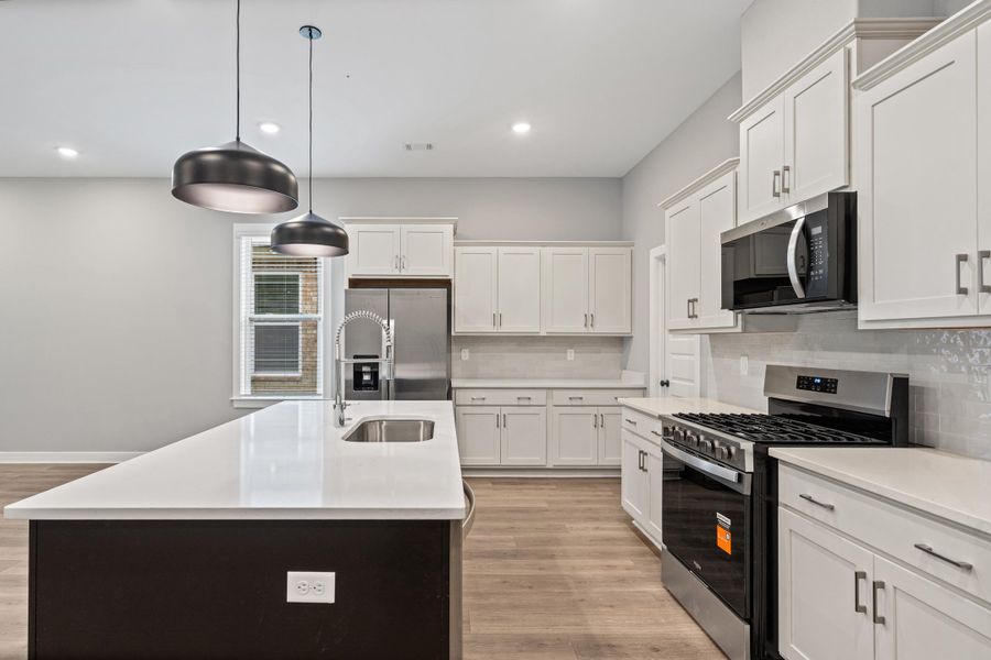 Spacious kitchen featuring white cabinetry, light-toned countertops, and wood-finish flooring Spacious kitchen featuring white cabinetry, light-toned countertops, and wood-finish flooring