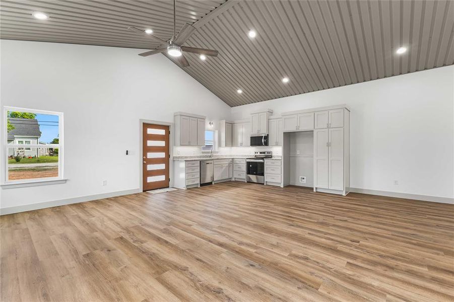 Unfurnished living room featuring high vaulted ceiling, baseboards, ceiling fan, light wood-type flooring, and recessed lighting Unfurnished living room featuring high vaulted ceiling, baseboards, ceiling fan, light wood-type flooring, and recessed lighting