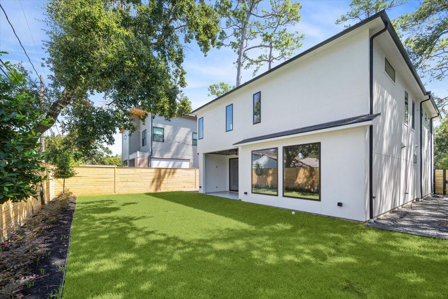 The rear elevation highlights the home’s contemporary architecture, with expansive glass doors and clean lines that blur the boundary between inside and out. A private wood fence frames the lush lawn, offering abundant space for recreation or the addition of a pool, garden, or play area. Designed with both style and livability in mind, the backyard is equally suited for entertaining or peaceful relaxation.
