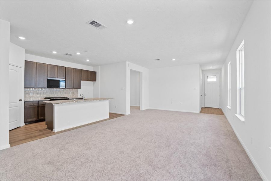 Designed for comfort and connection, this spacious open-concept great room boasts soaring ceilings, large windows with blinds, recessed lighting, and French Oak vinyl plank flooring, seamlessly merging with the stunning kitchen for easy living and entertaining.