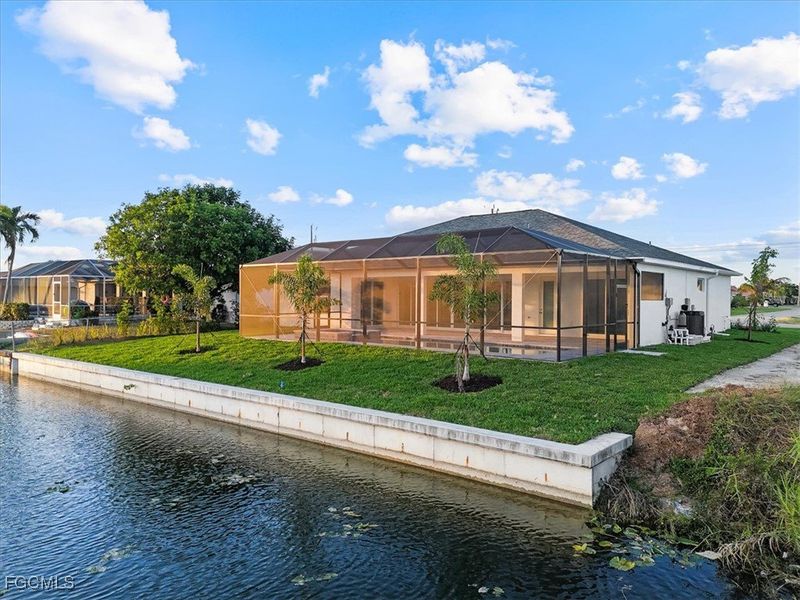 Back of property with a water view, a yard, glass enclosure, and a sunroom
