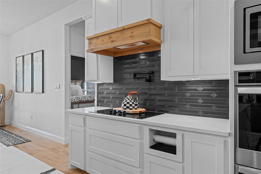 Kitchen with light stone countertops, light wood-type flooring, tasteful backsplash, white cabinetry, and stainless steel appliances