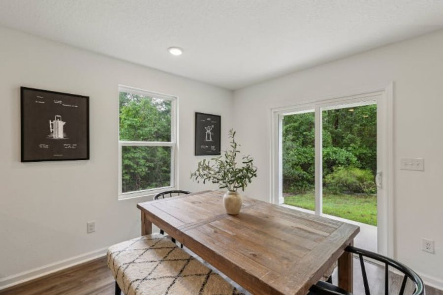 A table with a vase of flowers on it in a room with windows.