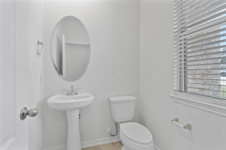 The powder room on the first floor includes a pedestal sink, mirror, toilet, and window with privacy blinds.