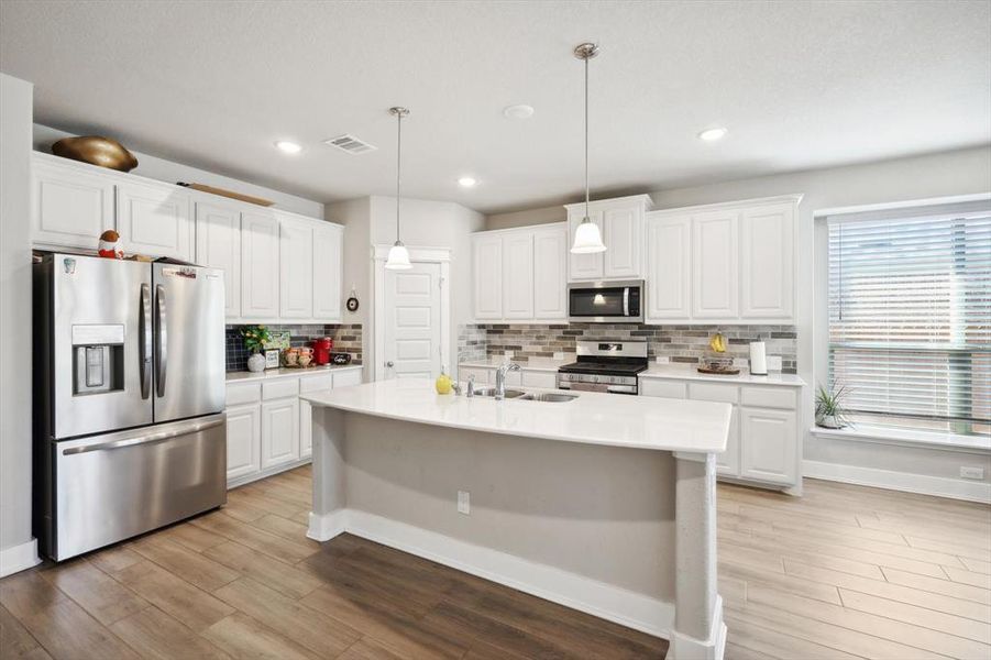 Kitchen featuring white cabinets, stainless steel appliances, tasteful backsplash, and decorative light fixtures