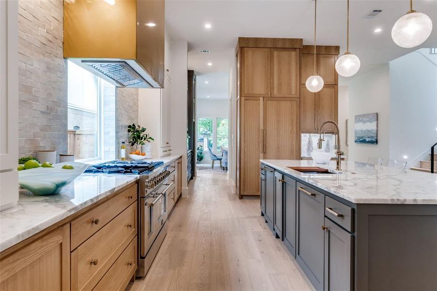 Kitchen with high end stainless steel range oven, light stone counters, visible vents, a sink, and light wood-type flooring Kitchen with high end stainless steel range oven, light stone counters, visible vents, a sink, and light wood-type flooring