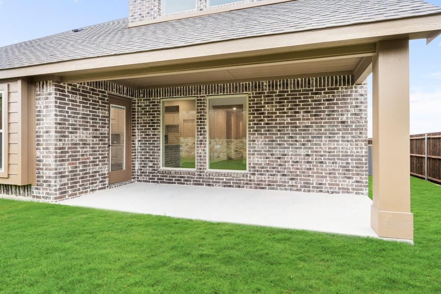 Covered back patio with concrete slab, brick exterior wall, large window, and green lawn with wood privacy fence Covered back patio with concrete slab, brick exterior wall, large window, and green lawn with wood privacy fence