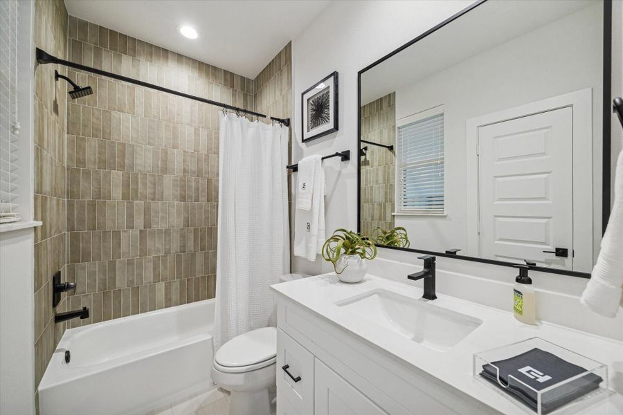 Ensuite bathroom featuring a quartz-topped vanity, matte black fixtures, and a tub-shower combo with warm vertical tile for a modern, spa-inspired finish. Ensuite bathroom featuring a quartz-topped vanity, matte black fixtures, and a tub-shower combo with warm vertical tile for a modern, spa-inspired finish.