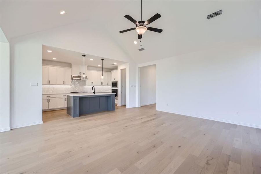 Unfurnished living room featuring light hardwood / wood-style floors, high vaulted ceiling, sink, and ceiling fan