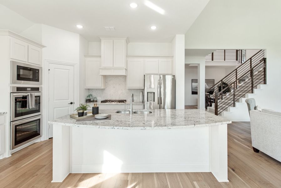 Open kitchen with white cabinets, large granite island, stainless steel appliances, and hardwood floors