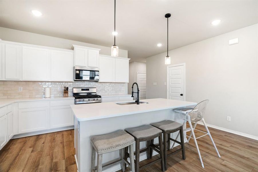 Kitchen with stainless steel appliances, decorative backsplash, hanging light fixtures, light wood-style floors, and recessed lighting Kitchen with stainless steel appliances, decorative backsplash, hanging light fixtures, light wood-style floors, and recessed lighting