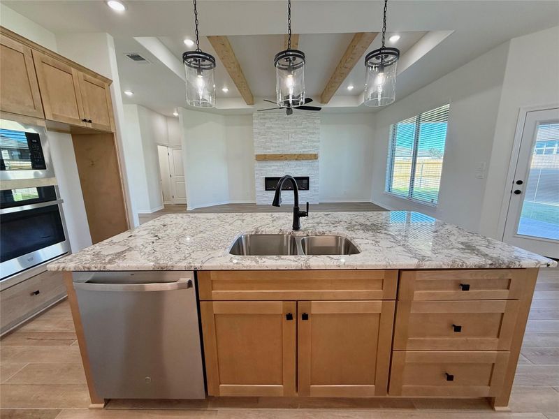 Kitchen featuring wood finish floors, pendant lighting, stainless steel appliances, light stone counters, and a stone fireplace