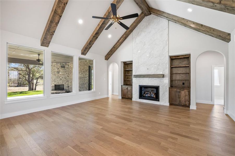 Unfurnished living room with arched walkways, a large fireplace, a ceiling fan, light wood-type flooring, and recessed lighting