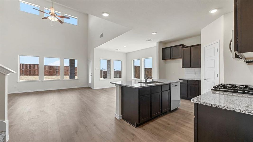 Kitchen featuring light stone counters, an island with sink, light wood-type flooring, open floor plan, and a high ceiling
