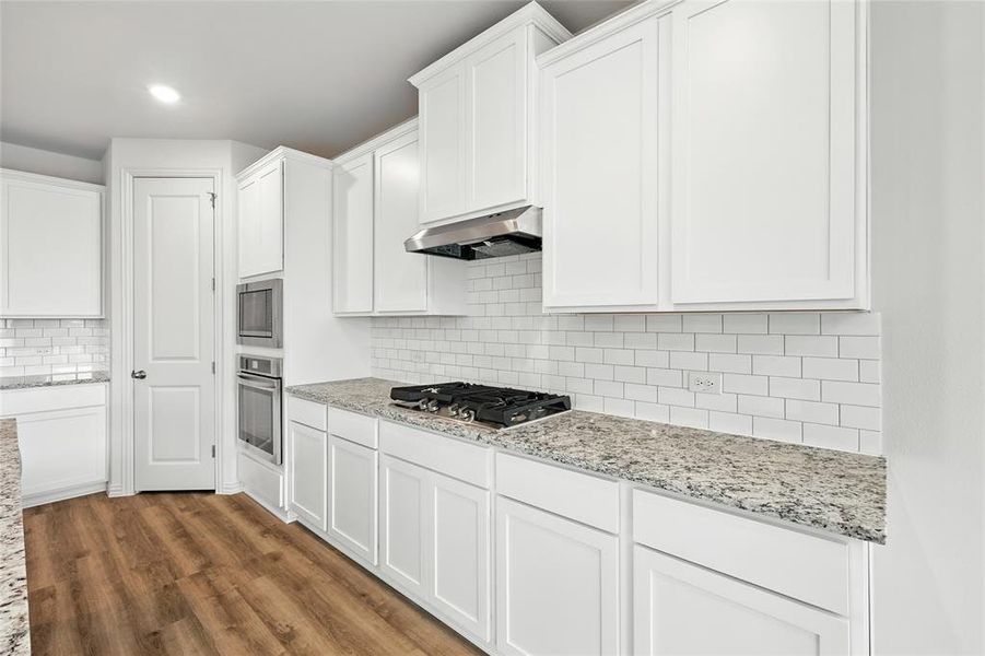 Kitchen with white cabinetry, dark wood-style flooring, light stone countertops, decorative backsplash, and recessed lighting Kitchen with white cabinetry, dark wood-style flooring, light stone countertops, decorative backsplash, and recessed lighting