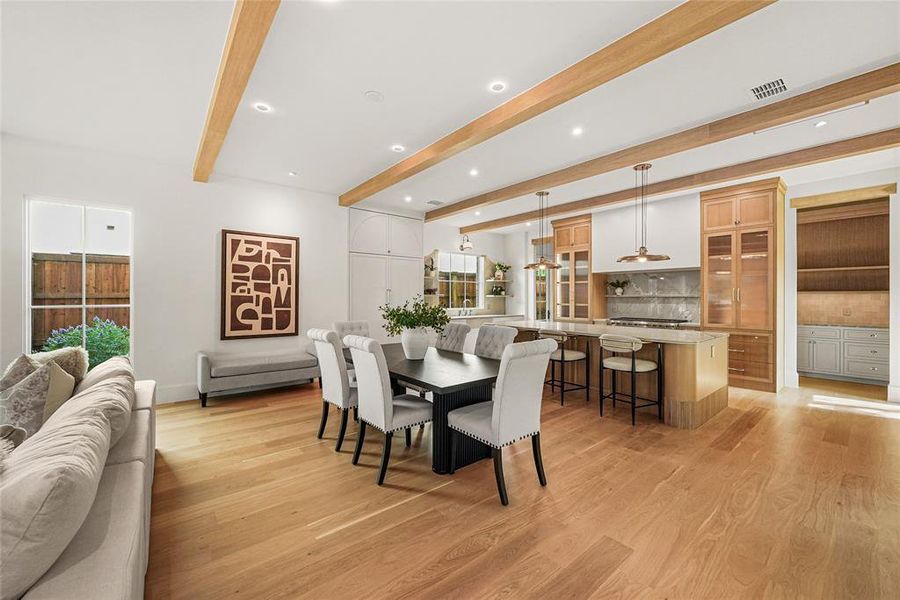 Spacious living area featuring light wood-finish flooring, exposed ceiling beams, recessed lighting, and a modern kitchen