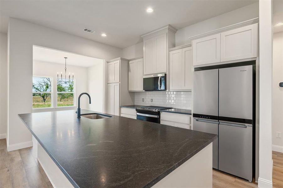 Kitchen with stainless steel appliances, light wood finished floors, a center island with sink, recessed lighting, and tasteful backsplash