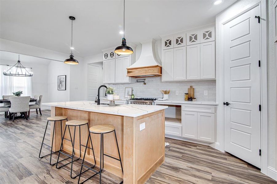 Kitchen featuring white cabinets, pendant lighting, a center island with sink, and premium range hood