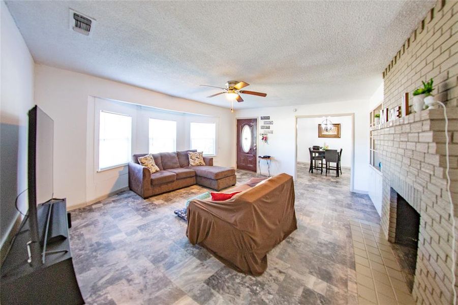 Living room with a textured ceiling, ceiling fan, and a brick fireplace