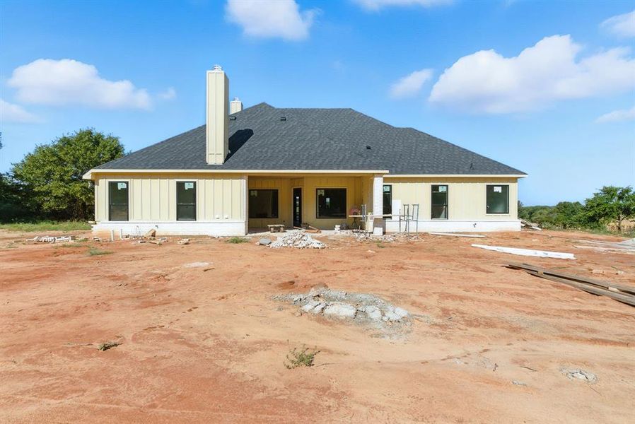 Rear view of house featuring a patio, a shingled roof, a chimney, and board and batten siding Rear view of house featuring a patio, a shingled roof, a chimney, and board and batten siding