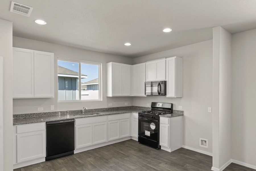 Image of home kitchen with white cabinets and black appliances. Wood-look floors, white walls, and a window over the sink