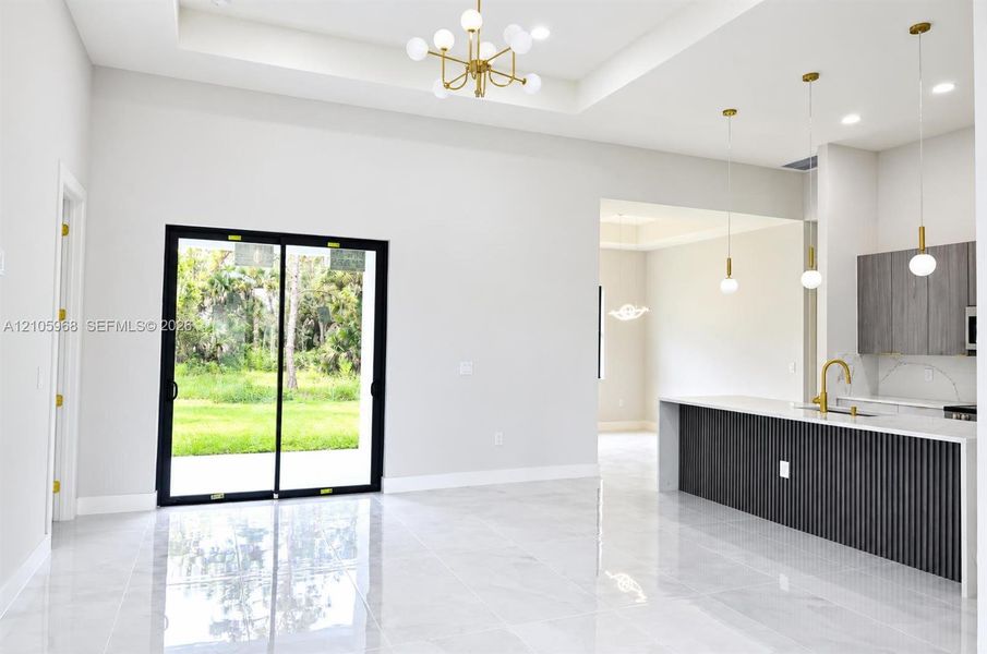 Open floor plan featuring a coffered ceiling, large-format tile flooring, a kitchen island with a slatted base, and black-frame sliding glass doors