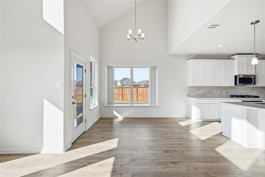 Kitchen featuring white cabinetry, high vaulted ceiling, decorative light fixtures, decorative backsplash, and a chandelier