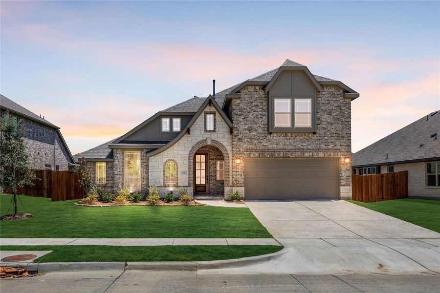 Two-story brick and stone home with arched entry, two-car garage, and manicured front lawn at dusk Two-story brick and stone home with arched entry, two-car garage, and manicured front lawn at dusk
