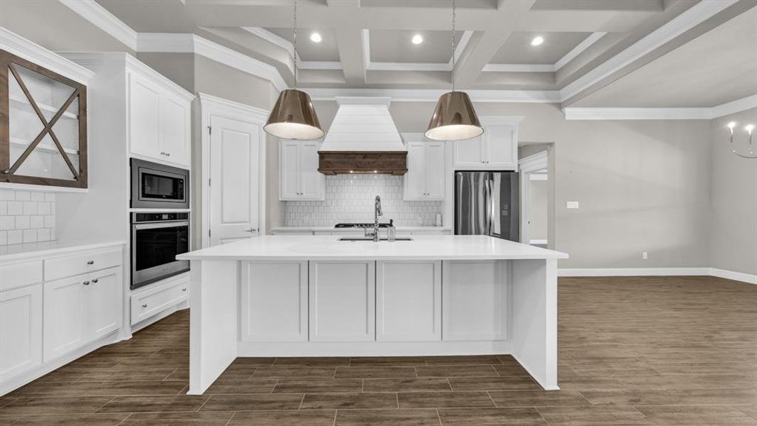 Kitchen with appliances with stainless steel finishes, coffered ceiling, a center island with sink, and decorative backsplash