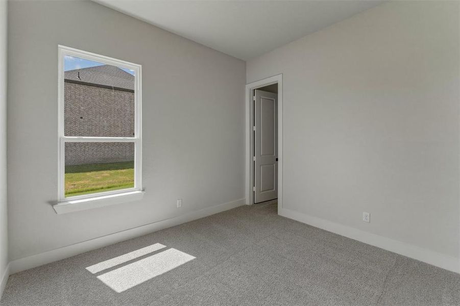 Room featuring neutral gray wall paint, gray carpet, white trim, a white window frame, and a white interior door with black hardware Room featuring neutral gray wall paint, gray carpet, white trim, a white window frame, and a white interior door with black hardware