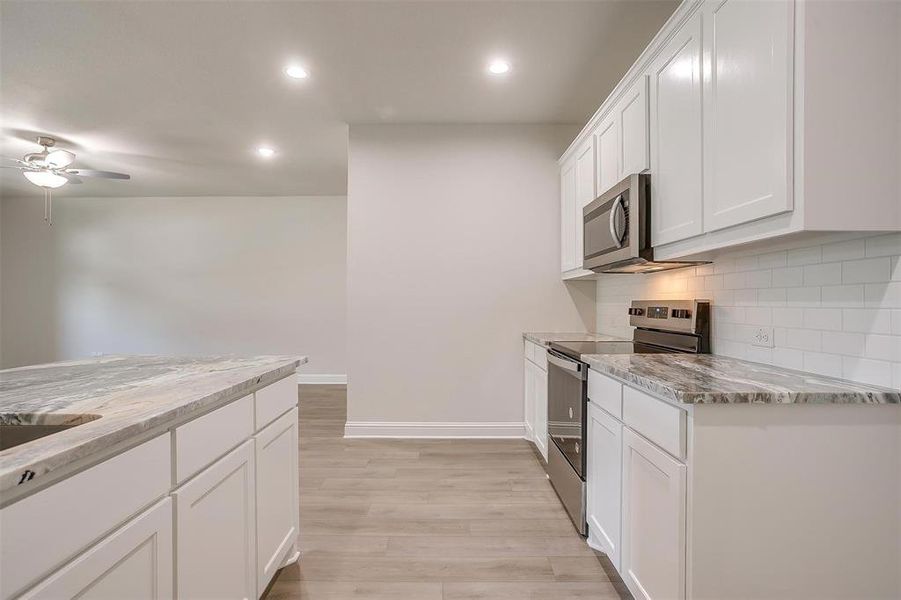 Kitchen featuring stainless steel appliances, white cabinets, decorative backsplash, light stone counters, and recessed lighting Kitchen featuring stainless steel appliances, white cabinets, decorative backsplash, light stone counters, and recessed lighting