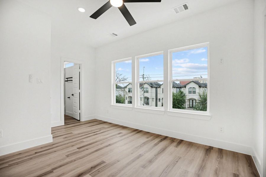 Bright room with large windows, wood-look flooring, and a ceiling fan. Ideal for a bedroom or office.