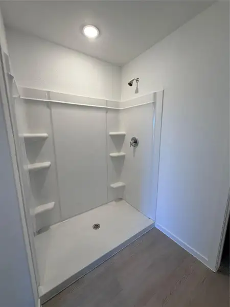 Bathroom with dark wood-style flooring, a textured wall, and a shower stall Bathroom with dark wood-style flooring, a textured wall, and a shower stall
