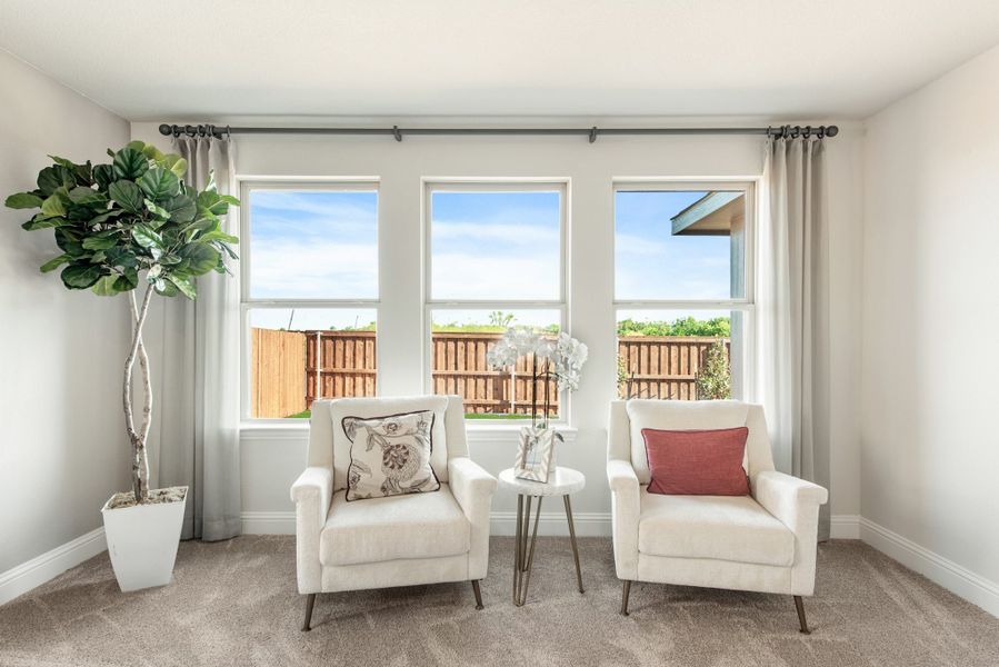 Sitting area with two white armchairs, small side table, and three windows overlooking a fenced backyard