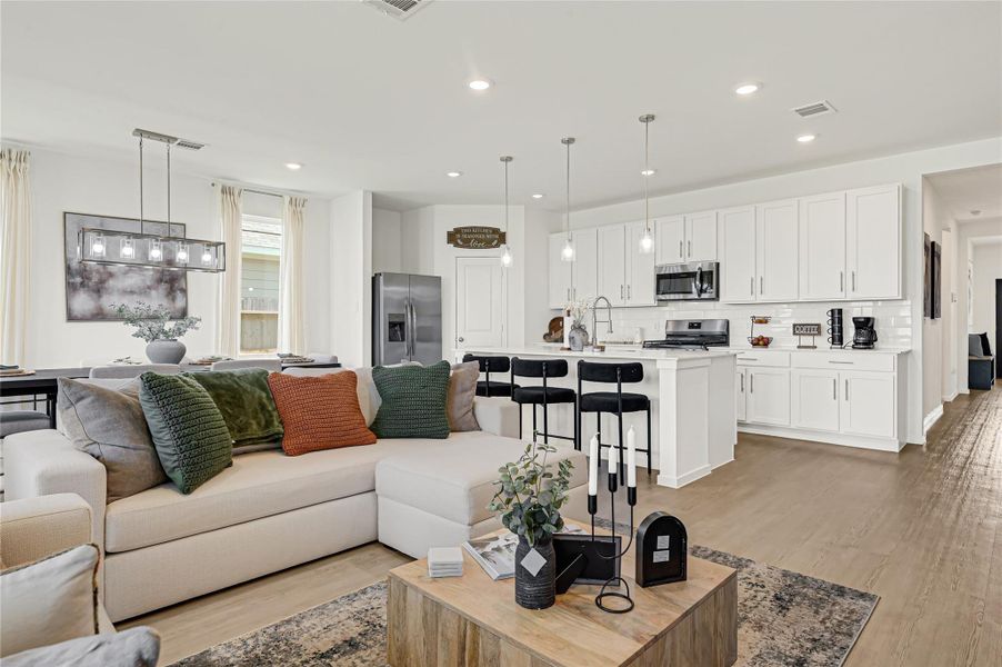 Bright and open living space with a modern kitchen featuring white cabinetry, stainless steel appliances, and a spacious island with seating, seamlessly flowing into the cozy living area. Bright and open living space with a modern kitchen featuring white cabinetry, stainless steel appliances, and a spacious island with seating, seamlessly flowing into the cozy living area.