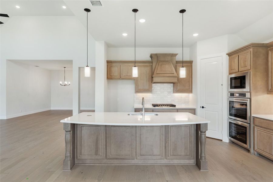 Large kitchen island with white countertop, wood cabinets, custom range hood, and double wall ovens Large kitchen island with white countertop, wood cabinets, custom range hood, and double wall ovens