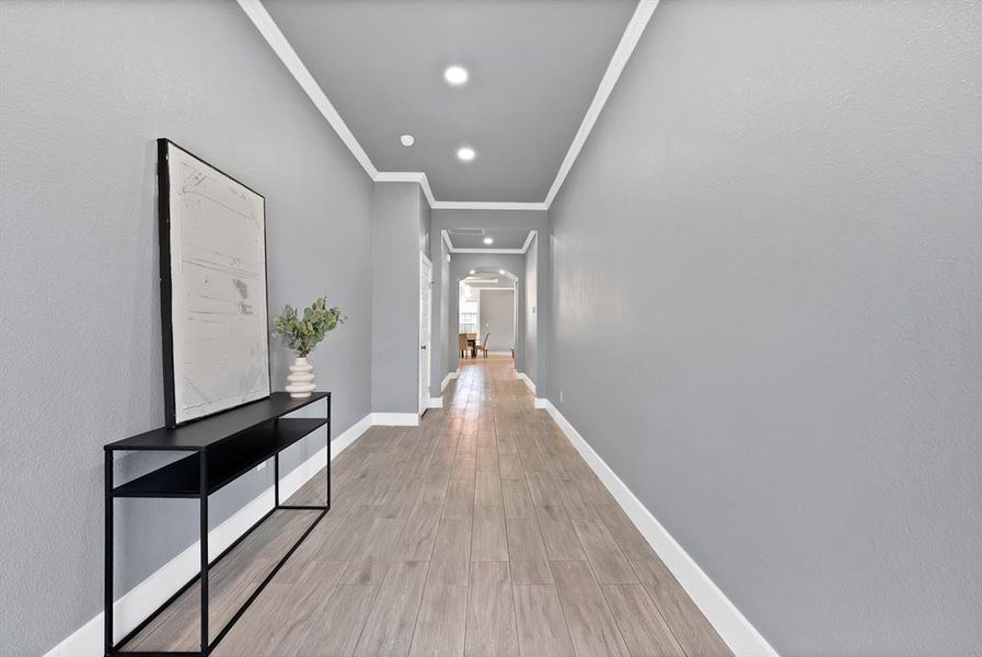 Hallway featuring wood-finish flooring, light gray walls, recessed lighting, white baseboards, and crown molding